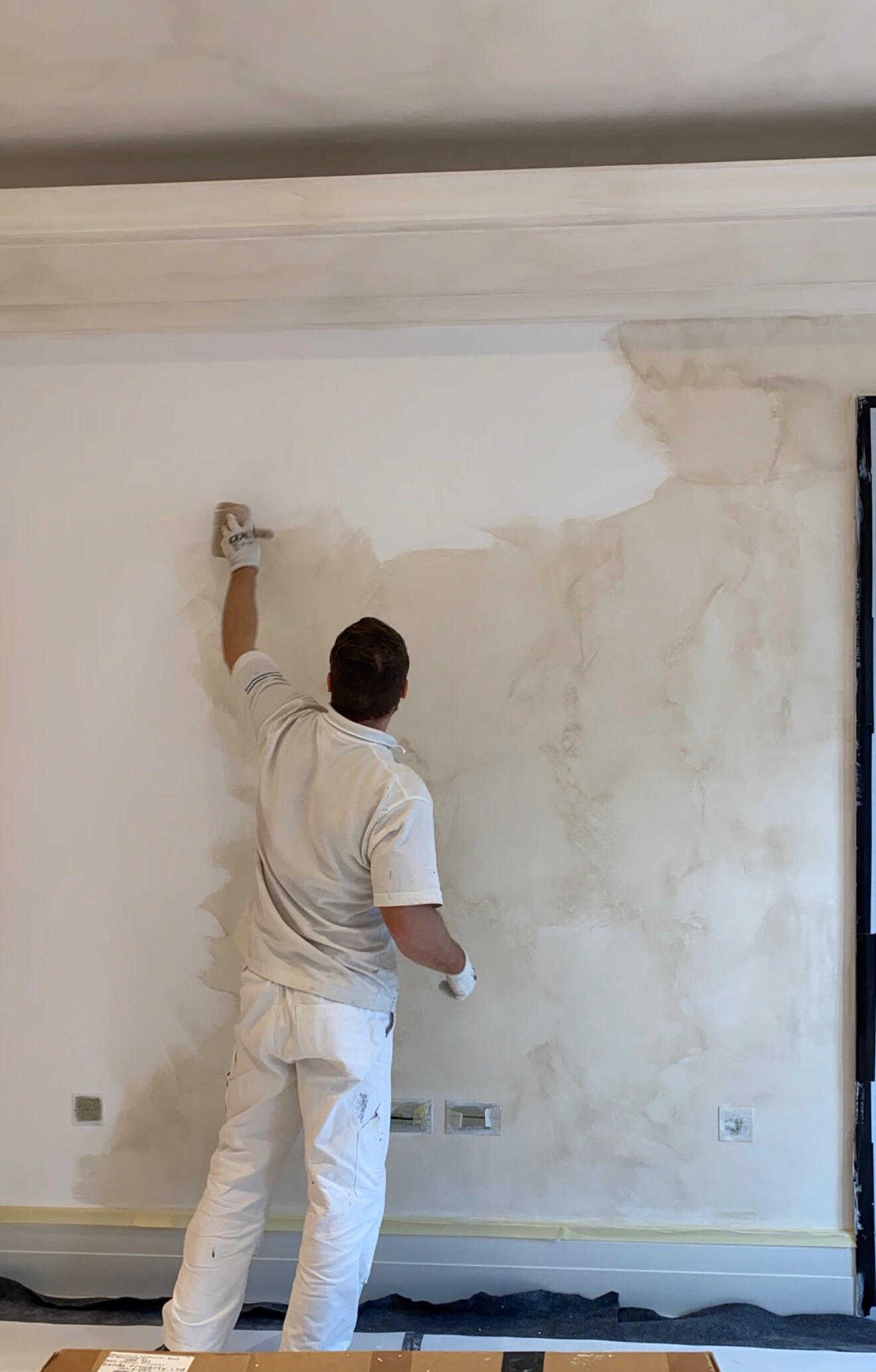 Applicator in whites trowelling limewash onto a wall in a London home, half finished surface showing the working edge