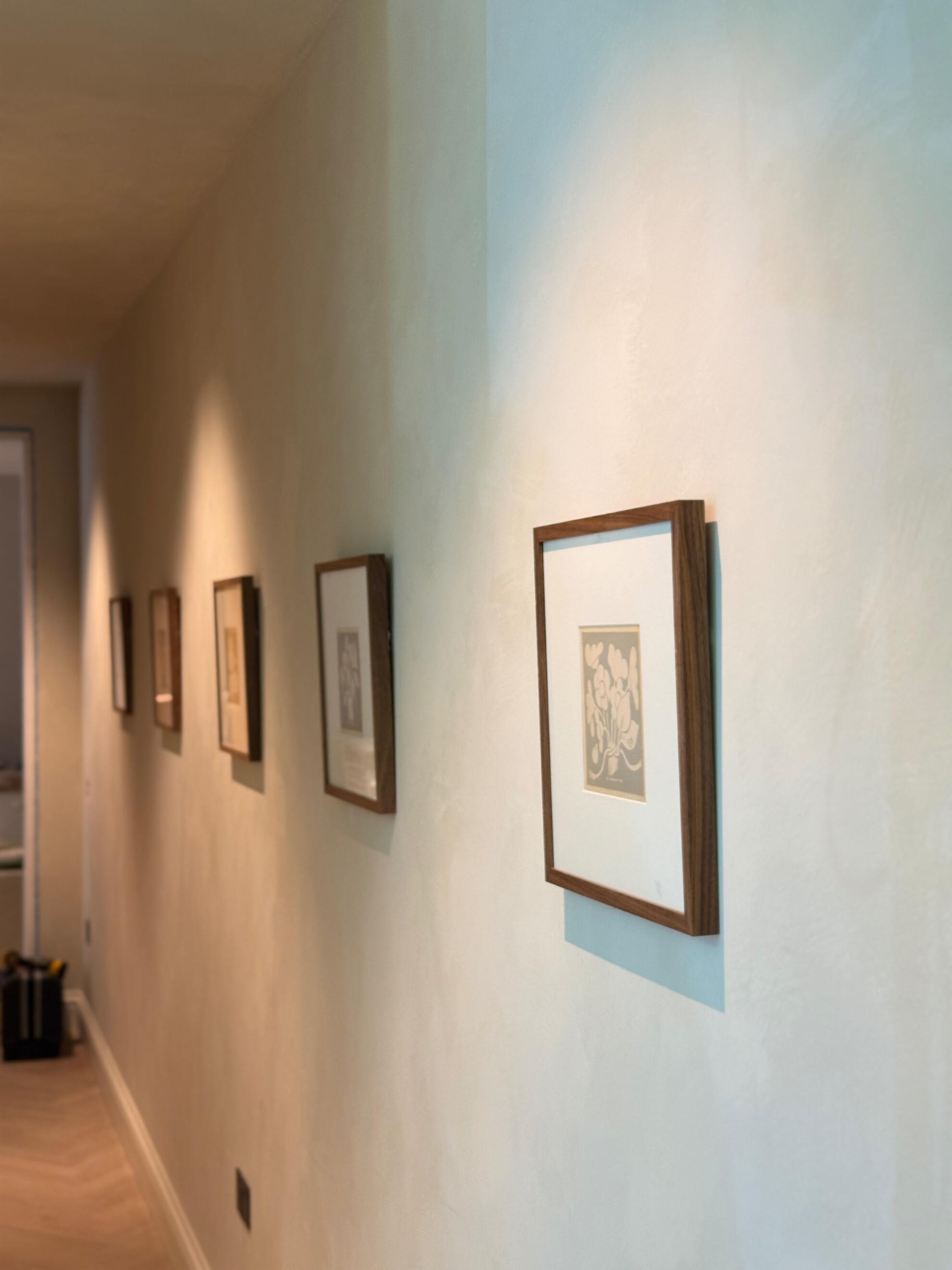 Limewashed hallway wall in a North London home, framed prints in raking light